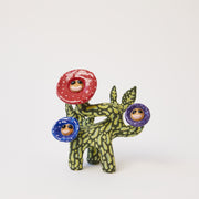 Sculpture of a thick flower stem with 3 different colored flowers: red, blue and purple. Each flower has a face as its center and sprouts from a different location.