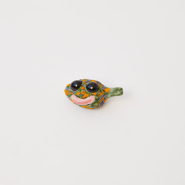 Ceramic sculpture of a bud of weed with a smiling face on it with large black glossy eyes. 