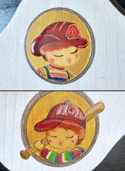 Close up of 2 painted details on the plaque: a redhead child wearing a fireman's hat and a redhead child wearing a baseball cap and holding a bat.