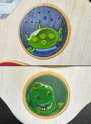 Close up of painted details on the plaque: the green alien from Toy Story with its eyes closed, making a kissy face and Rex.