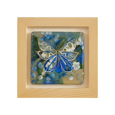 Painting of a line art butterfly, white and gold atop background of green lily pads and blue flowers. Piece is in wooden frame.