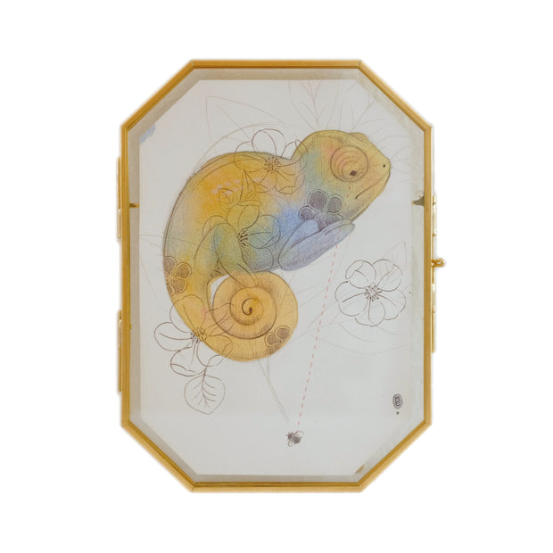 Illustration on octagon shaped paper of a yellow chameleon with blue accent coloring. Graphite details of flowers and a small bug are nearby. 