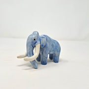 Ceramic sculpture of a blue mammoth, with large curved tusks and a long nose that touches the ground.