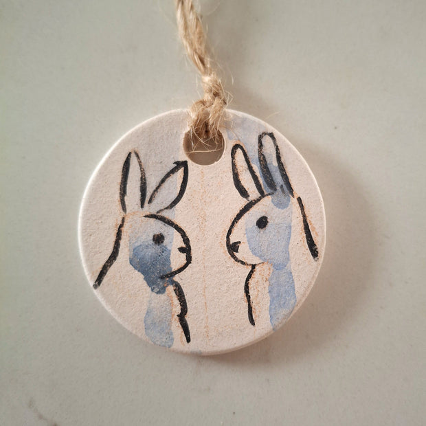 Illustration on rounded pennant of 2 rabbits, looking at one another with blue colored streaks running down their faces.