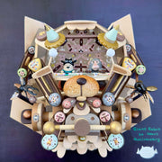 Mixed media sculpture of a cute cartoon person and a monkey piloting an open air plane shaped like a cats head, with many attached parts and pieces and a snout in the center. Bugs fly around it.