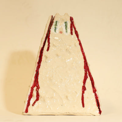 Offwhite ceramic sculpture of a pyramid shaped vase, with a wide base and a slightly narrow top. The vase is bumpy in texture and has a subtle cat face on the top. It has streaks of red running down the side of it.