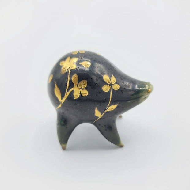 Rounded dark greenish blue ceramic sculpture of a quadruped with short legs and small gold eyes over a goofy open mouth smile. Its body features a gold flower pattern.