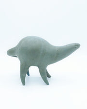 Ceramic sculpture of a rounded body character, a muted teal in color with  simple line smile and small eyes. It has a long neck and a long skinny tail.