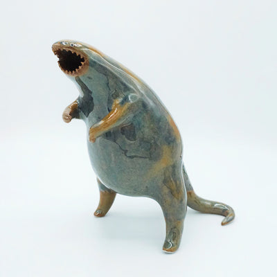 Glazed ceramic sculpture of a large rounded body monster, standing on hind legs with many small teeth and an open mouth. Colors are blue with brown accent coloring.