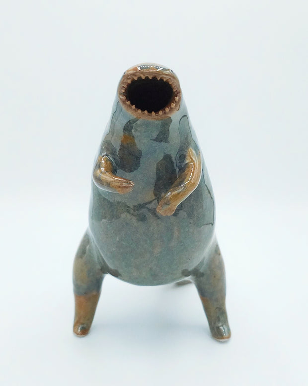 Glazed ceramic sculpture of a large rounded body monster, standing on hind legs with many small teeth and an open mouth. Colors are blue with brown accent coloring.