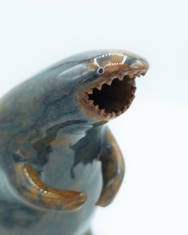 Glazed ceramic sculpture of a large rounded body monster, standing on hind legs with many small teeth and an open mouth. Colors are blue with brown accent coloring.