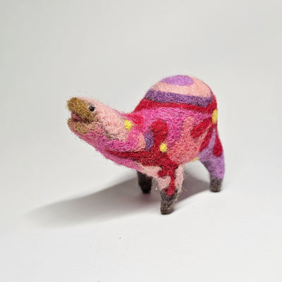 Needle felted wool sculpture of a pink rounded body quadruped creature with an open mouth, goofy smile and small black dot eyes. Its body contains a pink, purple and red retro swirl and floral pattern.