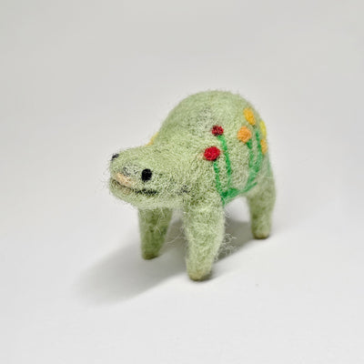 Needle felted wool sculpture of a light green rounded body quadruped creature with a cute smile and small black eyes. It has red, orange and yellow poppy flowers on its body.