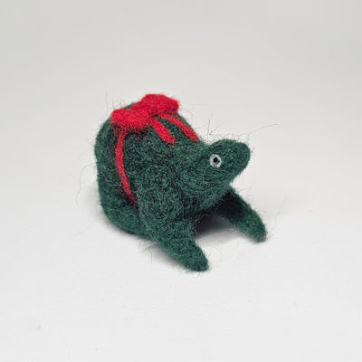 Needle felted wool sculpture of a dark green rounded body quadruped creature with a cute smile and small black eyes. It sits on its hind legs and has a red bow wrapped around its body, as though its a present.