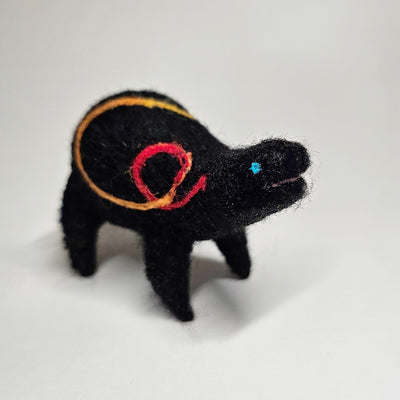 Felted sculpture of a black rounded body quadruped creature with a cute open mouth and bright blue dot eyes. It has a thread of red to orange to yellow ribbon spiraling across its body.