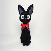 Needle felt wool sculpture of Jiji the cat from Kiki's Delivery Service, wearing a red bow around its neck and sitting with very straight posture.