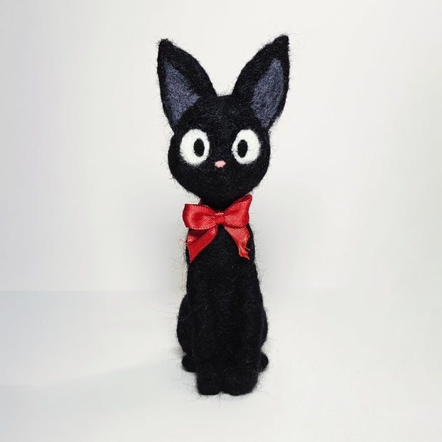 Needle felt wool sculpture of Jiji the cat from Kiki's Delivery Service, wearing a red bow around its neck and sitting with very straight posture.