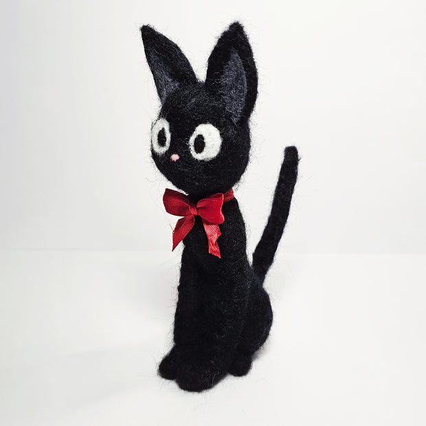 Needle felt wool sculpture of Jiji the cat from Kiki's Delivery Service, wearing a red bow around its neck and sitting with very straight posture.