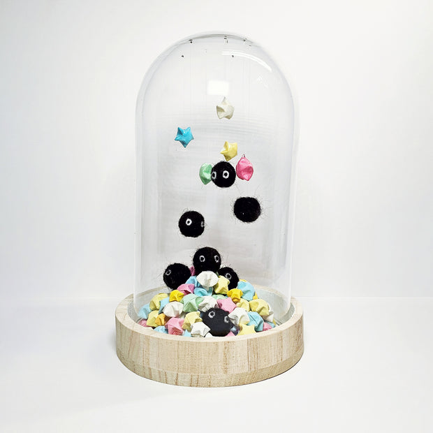 Glass cloche with a wooden bottom containing many small sculptures of black soot sprites made out of wool. They hang from the top of the glass and are surrounded by paper stars.