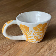 White ceramic mug with a large handle with a carved pattern of orange poppy flowers with matching orange leaves.