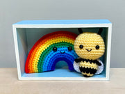 2 crocheted plushes: one of a rainbow and the other of a bee with a large cartoon like head. They both have black bead eyes and small smiles.