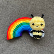 2 crocheted plushes: one of a rainbow and the other of a bee with a large cartoon like head. They both have black bead eyes and small smiles.