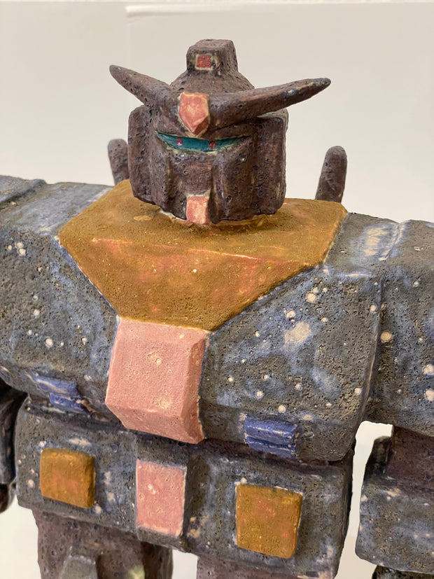 Ceramic sculpture of a Gundam with a wide, blocky body and several buttons and suit detailing with a pointed helmet.