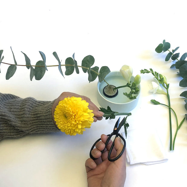 Overhead photo of someone assembling a flower arrangement, cutting the stems of flowers and placing them in a bowl. 