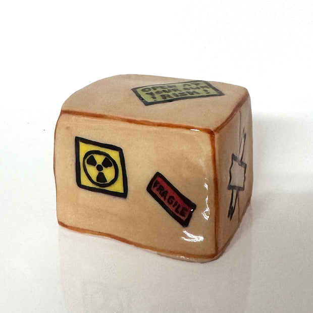 Ceramic sculpture of a cardboard box, with several caution or danger stickers.