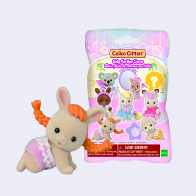 Small flocked figurine of a bunny like a human baby, crawling while wearing a pink laced diaper and with a cute smiling expression. They have an orange, long braided wig and are in front of their product packaging.