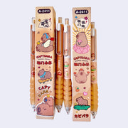 Collection of several gel pens with brown bodies, a rounded metal clip and a squishy barreled surface for placing one's hand. Small illustrations of cartoon capybaras are on the pens and product packaging.