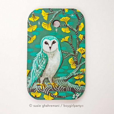 Painting of a turquoise colored owl standing on a branch of a gingko tree with yellow leaves. Background is teal blue.