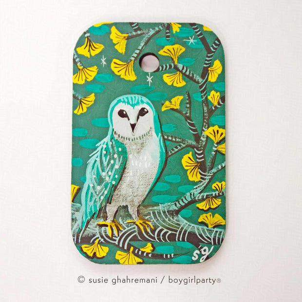 Painting of a turquoise colored owl standing on a branch of a gingko tree with yellow leaves. Background is teal blue.