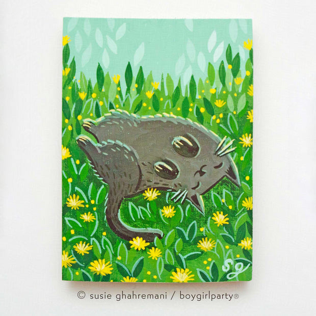 Painting of a gray cat, smiling and rolling around in grass with yellow dandelions.