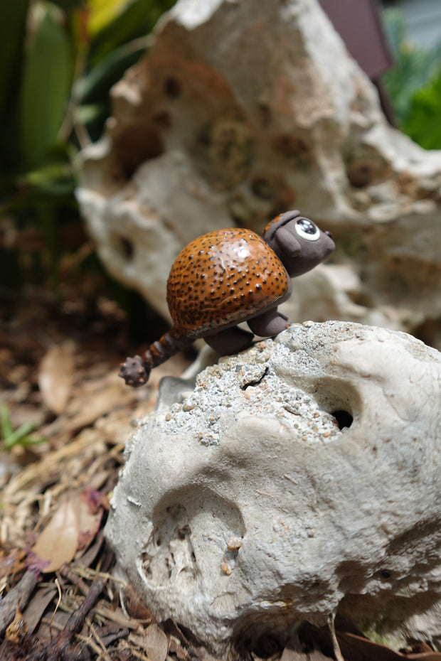 Small ceramics sculpture of a brown Ankylosaurus, with large cute eyes and a dotted outer shell. 