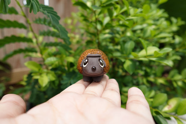 Small ceramics sculpture of a brown Ankylosaurus, with large cute eyes and a dotted outer shell. 