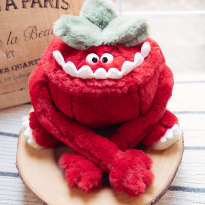 Plush doll of a furry tomato, with a large underbite smile and cute, small plastic eyes.