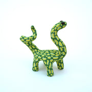 Ceramic sculpture of a green long neck dinosaur with large light green splotches as a pattern. It has a spiraled tail and black shiny eyes.