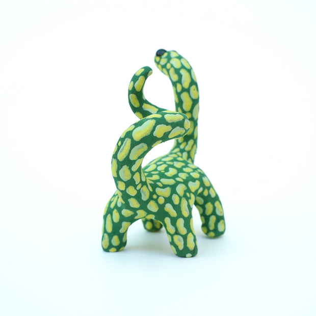 Ceramic sculpture of a green long neck dinosaur with large light green splotches as a pattern. It has a spiraled tail and black shiny eyes.