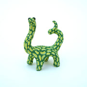 Ceramic sculpture of a green long neck dinosaur with large light green splotches as a pattern. It has a spiraled tail and black shiny eyes.