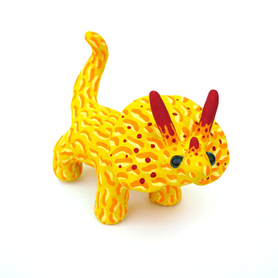 Ceramic sculpture of a yellow stegosaurus dinosaur with an orange squiggly line pattern. It has red tipped horns and small blacks shiny eyes. 