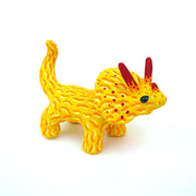 Ceramic sculpture of a yellow stegosaurus dinosaur with an orange squiggly line pattern. It has red tipped horns and small blacks shiny eyes. 