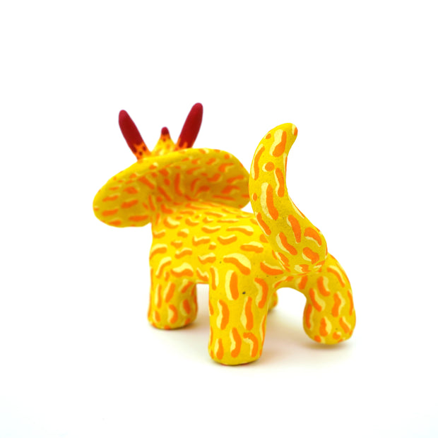 Ceramic sculpture of a yellow stegosaurus dinosaur with an orange squiggly line pattern. It has red tipped horns and small blacks shiny eyes. 