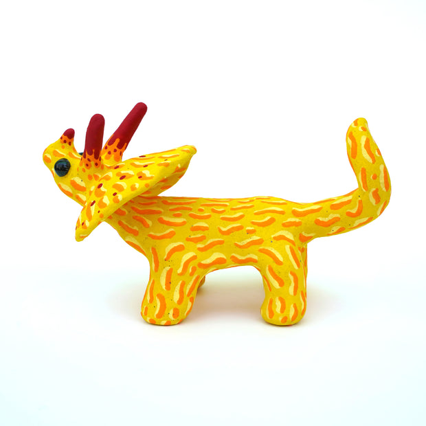 Ceramic sculpture of a yellow stegosaurus dinosaur with an orange squiggly line pattern. It has red tipped horns and small blacks shiny eyes. 