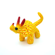 Ceramic sculpture of a yellow stegosaurus dinosaur with an orange squiggly line pattern. It has red tipped horns and small blacks shiny eyes. 