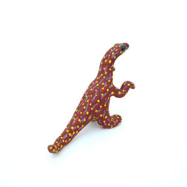 Ceramic sculpture of a red velociraptor with a pattern of red and purple squiggles on its body and many yellow polka dots. It has large shiny black eyes.