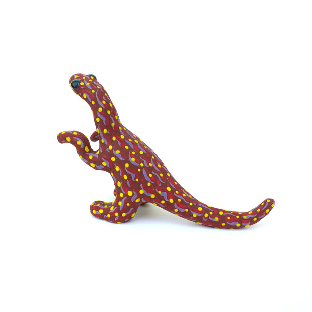 Ceramic sculpture of a red velociraptor with a pattern of red and purple squiggles on its body and many yellow polka dots. It has large shiny black eyes.