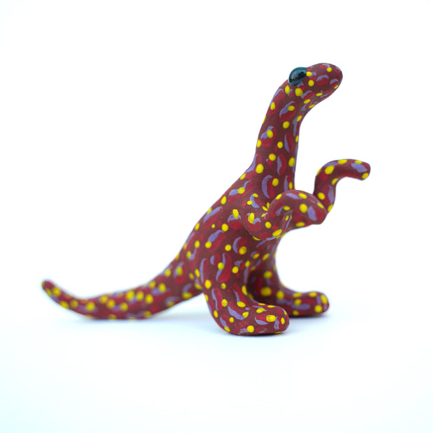 Ceramic sculpture of a red velociraptor with a pattern of red and purple squiggles on its body and many yellow polka dots. It has large shiny black eyes.