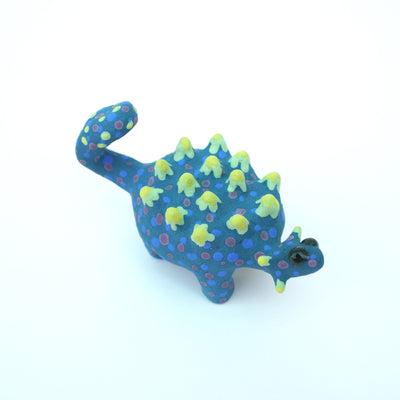 Sculpture of a blue stylized Ankylosaurus with neon green spikes and blue and purple polka dots on its body. It has a long tail and large shiny eyes.