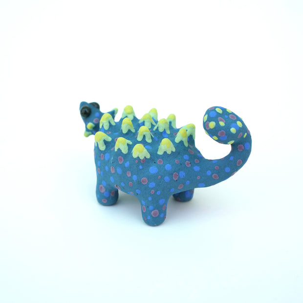 Sculpture of a blue stylized Ankylosaurus with neon green spikes and blue and purple polka dots on its body. It has a long tail and large shiny eyes.